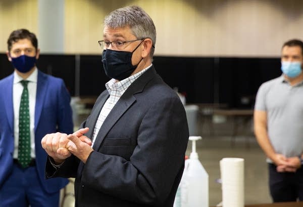 three men stand in a room wearing masks