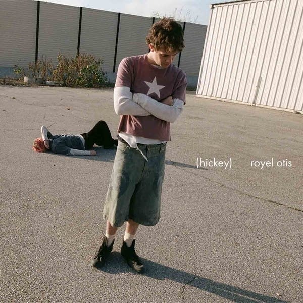 One man standing on a paved area while another lies on the paving behind him