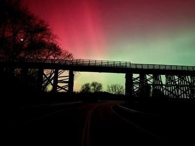 Reds and greens paint the sky behind a lifted bridge over a road.