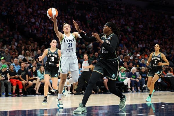 A basketball player in white jumps for a shot while facing off against an opposing player.