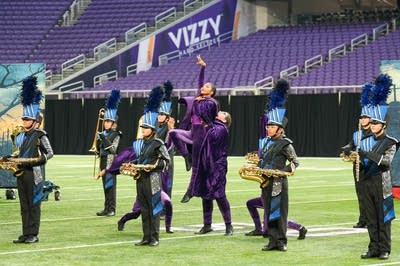 A marching band performs on the field of a football stadium.