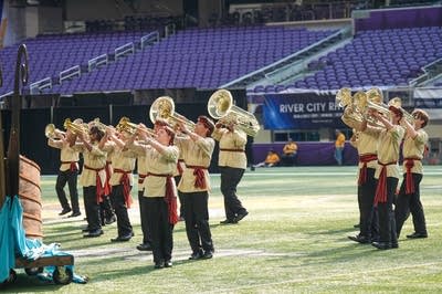 A marching band performs on the field of a football stadium.
