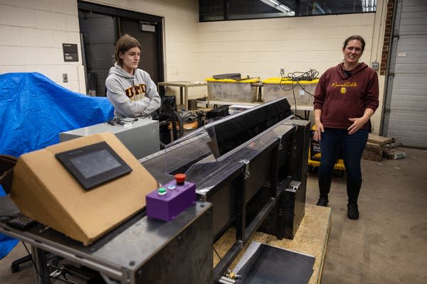 Two people stand next to a large shredding machine