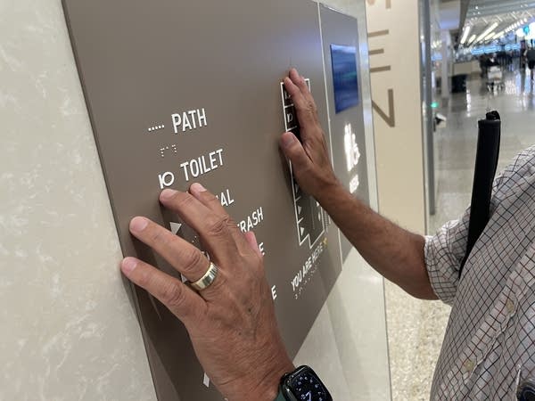 A man holds his hands up to feel a map on the wall.