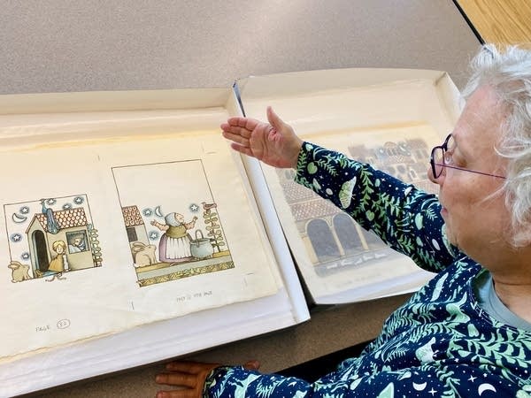 A woman gestures to a set of drawings preserved in a library.
