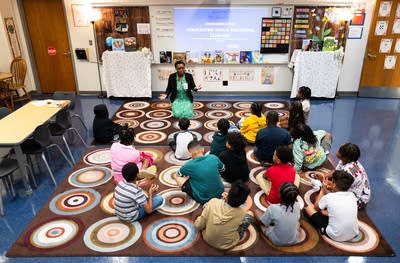 Students sit on rugs in a classroom