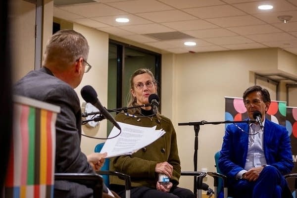 Three people sit on a stage and talk.