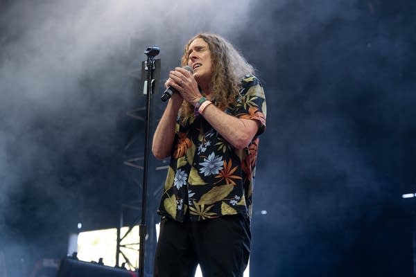 A man sings into a microphone on an outdoor stage