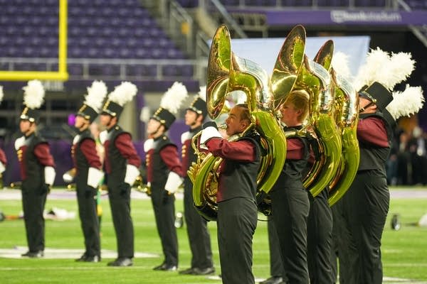A marching band performs on the field of a football stadium.