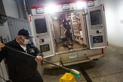 Two EMS workers mop and sweep the back of an ambulance.