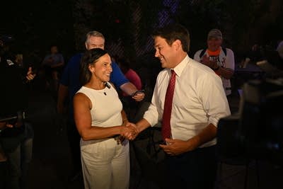 A woman in white and a man in a red tie stand in the middle of a dark crowd.