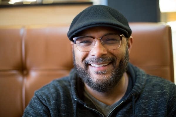 A person smiling while wearing glasses and a hat.