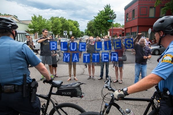 Protesters hold signs in front of police. 