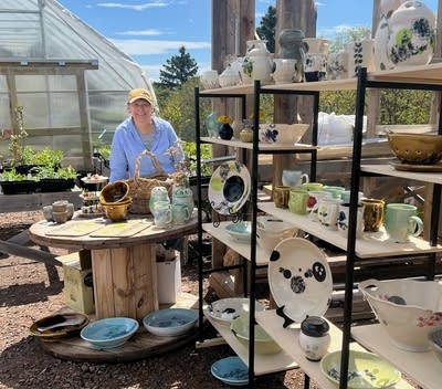 A woman stands near a display of pottery.