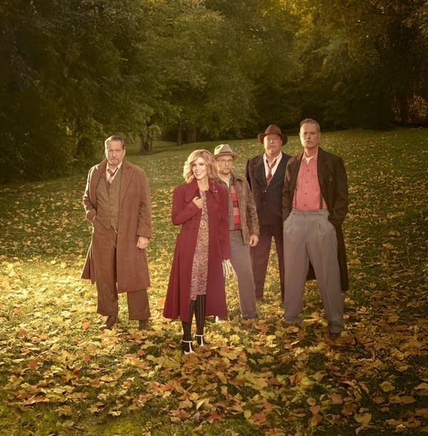 Five people in long coats standing in a field of autumn leaves