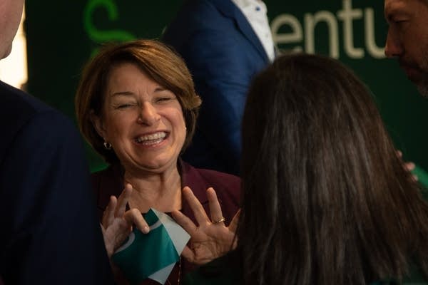 Sen. Amy Klobuchar waves after a ribbon cutting ceremony, holding a piece of ribbon.