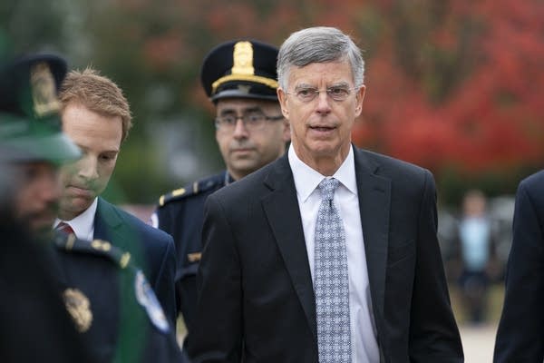 A man in a suit is escorted by security