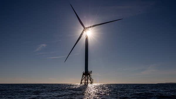 The sun behind a wind turbine in the ocean.