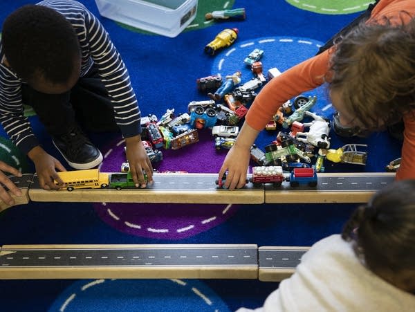 Three kids play with toy trains and cars.