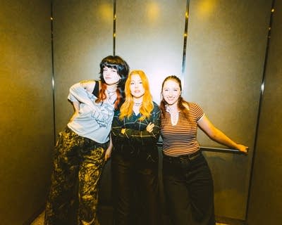 Three musicians stand together for a portrait in an elevator