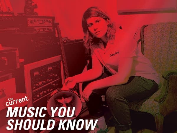 A woman sits in a chair holding a tambourine in a room with recording gear