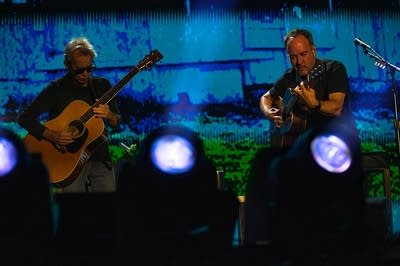 Two musicians play acoustic guitars on a large outdoor stage