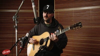 A man sings and plays guitar in a recording studio