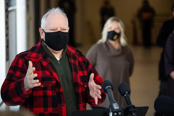 A man in a red checkered shirt speaks at a microphone.