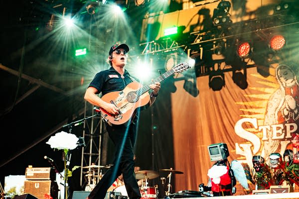 A musician sings and plays guitar on an outdoor stage