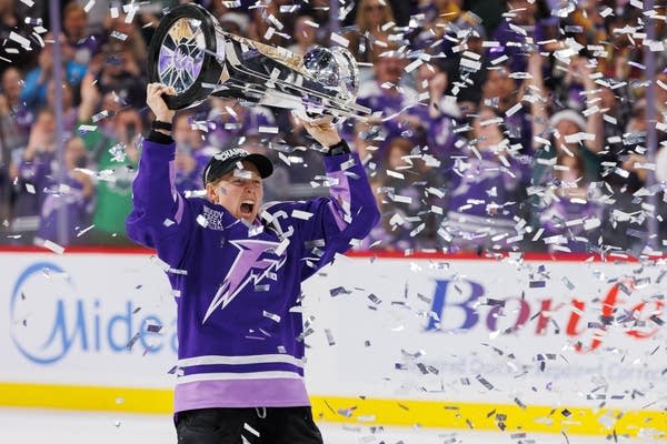A hockey player holds a trophy above her head.