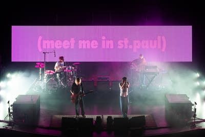 A four-piece band performing onstage in a large music venue