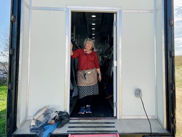 A woman poses for a photo while standing in the doorway to a wardrobe trailer.