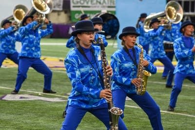A marching band performs on the field of a football stadium.