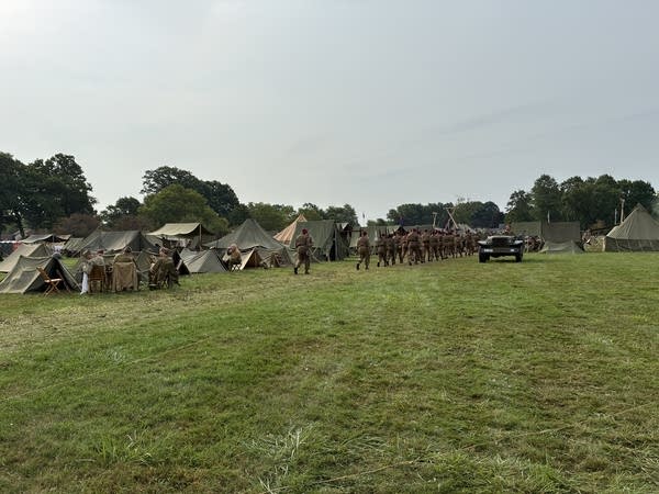 People representing the allied troops in WWII with red hats and green wool uniforms march through the allied camp back toward their tents.