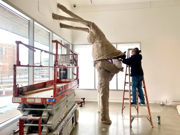 A person stands next to a sculpture on a ladder