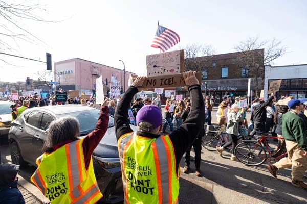 Protesters march down a street while holding signs.