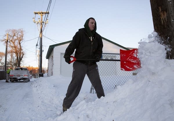 A man shoveling snow from a sidewalk.