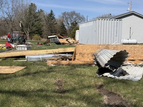 Debris and aluminum siding are spread across a yard.