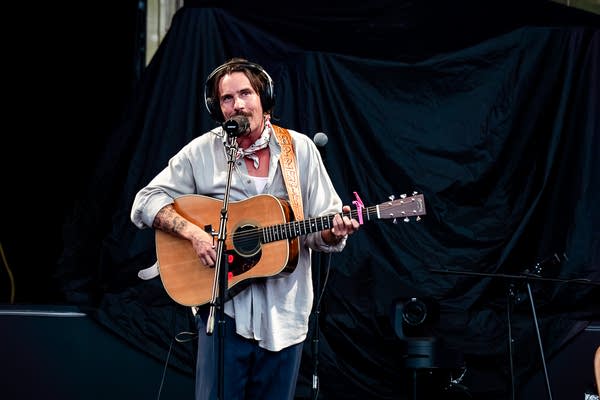 A musician sings and plays guitar on an outdoor stage