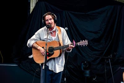 A musician sings and plays guitar on an outdoor stage
