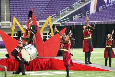 A marching band performs on the field of a football stadium.
