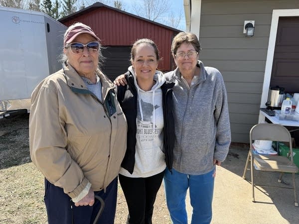 Three women pose for a photo in a driveway.