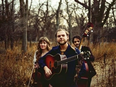 Three people with acoustic instruments stand outdoors 