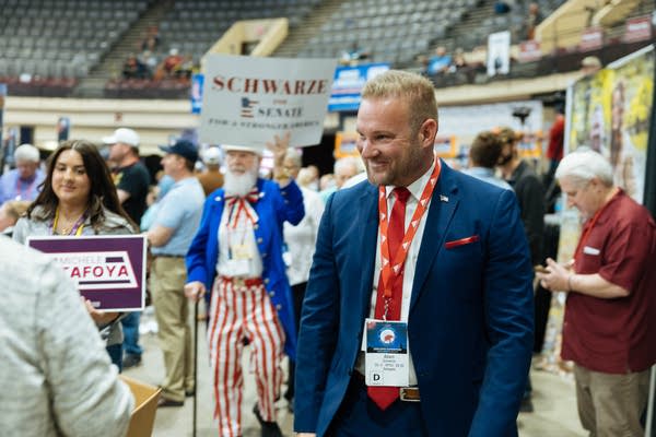 A man speaks with delegates while a man dressed in an Uncle Sam outfit carries a sign.