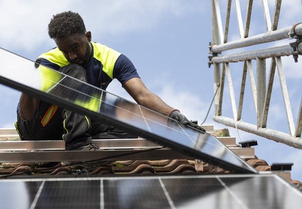 A man in a hi-vis vest installs a solar panel on a roof.