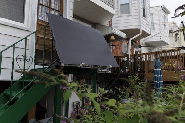 A large solar panel hangs off a staircase railing outside a house.