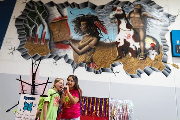 Two singers stand below a mural