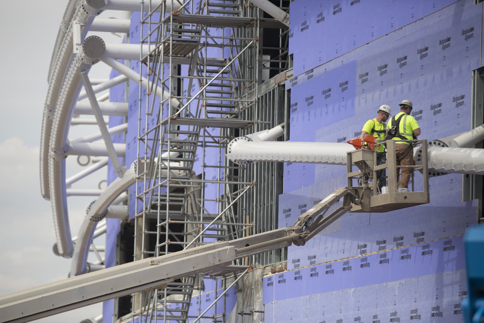 Construction workers fasten steel beams to the outside of the stadium.