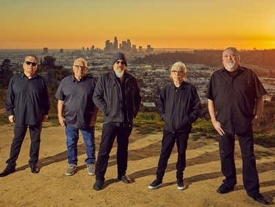 5 men stand at dusk with Los Angeles skyline in the background