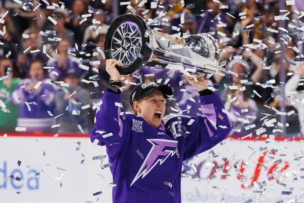 A hockey player holds a trophy above her head.